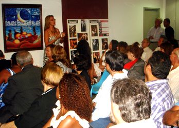 Sandra Serrado palestra com a exposição de fotos e quadros ao fundo